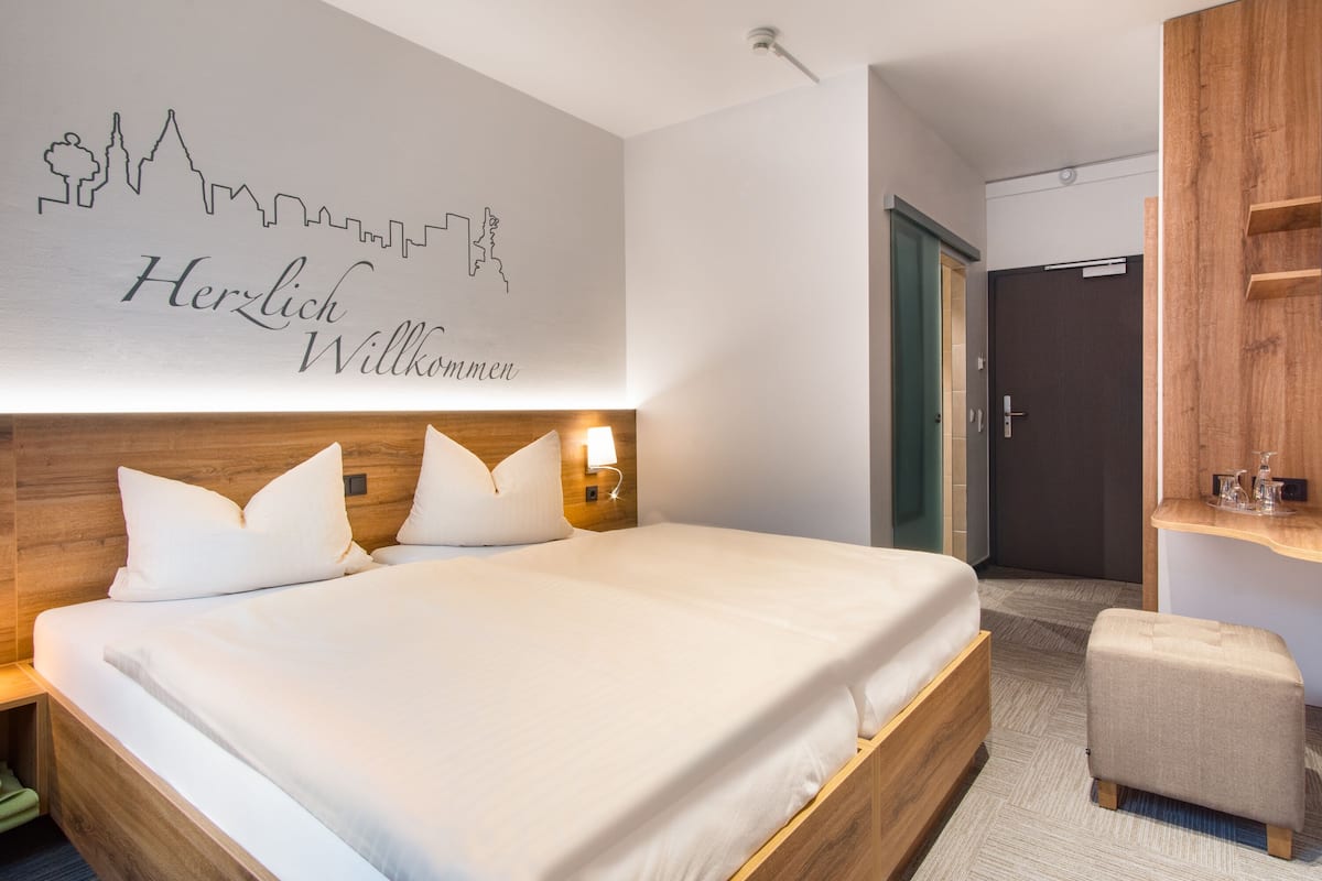 A hotel room with a large bed, a wooden headboard, a wall with a city skyline silhouette, and a small seating area.