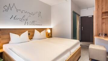 Une chambre d’hôtel avec un grand lit, une tête de lit en bois, un mur orné d’une silhouette représentant le profil d’une ville, et un petit coin salon.