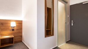 Habitación de hotel con cabecera de madera, lámpara de noche, espejo y puerta corredera.