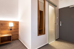 A hotel room with a wooden headboard, a bedside lamp, a mirror, and a sliding door.