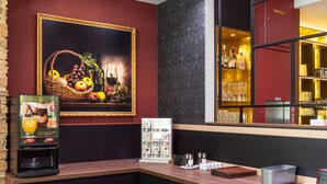 Una zona de bar con una cesta de fruta, un cuadro enmarco, un dispensador de bebidas y una vitrina de vidrio.