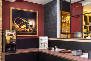 A bar area with a fruit basket, a framed painting, a beverage dispenser, and a glass display.