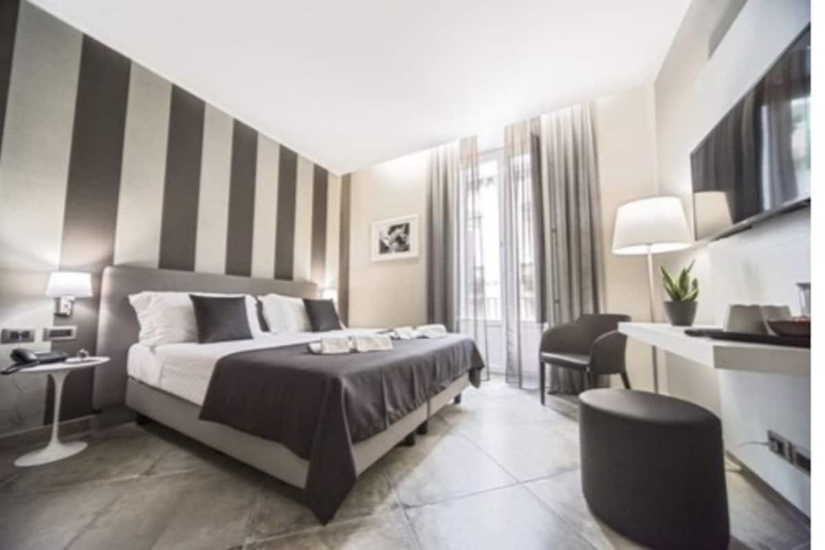 A modern hotel room with a large bed, bedside tables, a desk, and a TV.