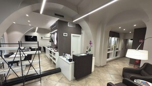 A modern interior with a reception desk, seating area, and a kitchen in the background. - Etnea 454   Catania Luxury Rooms (Catania)
