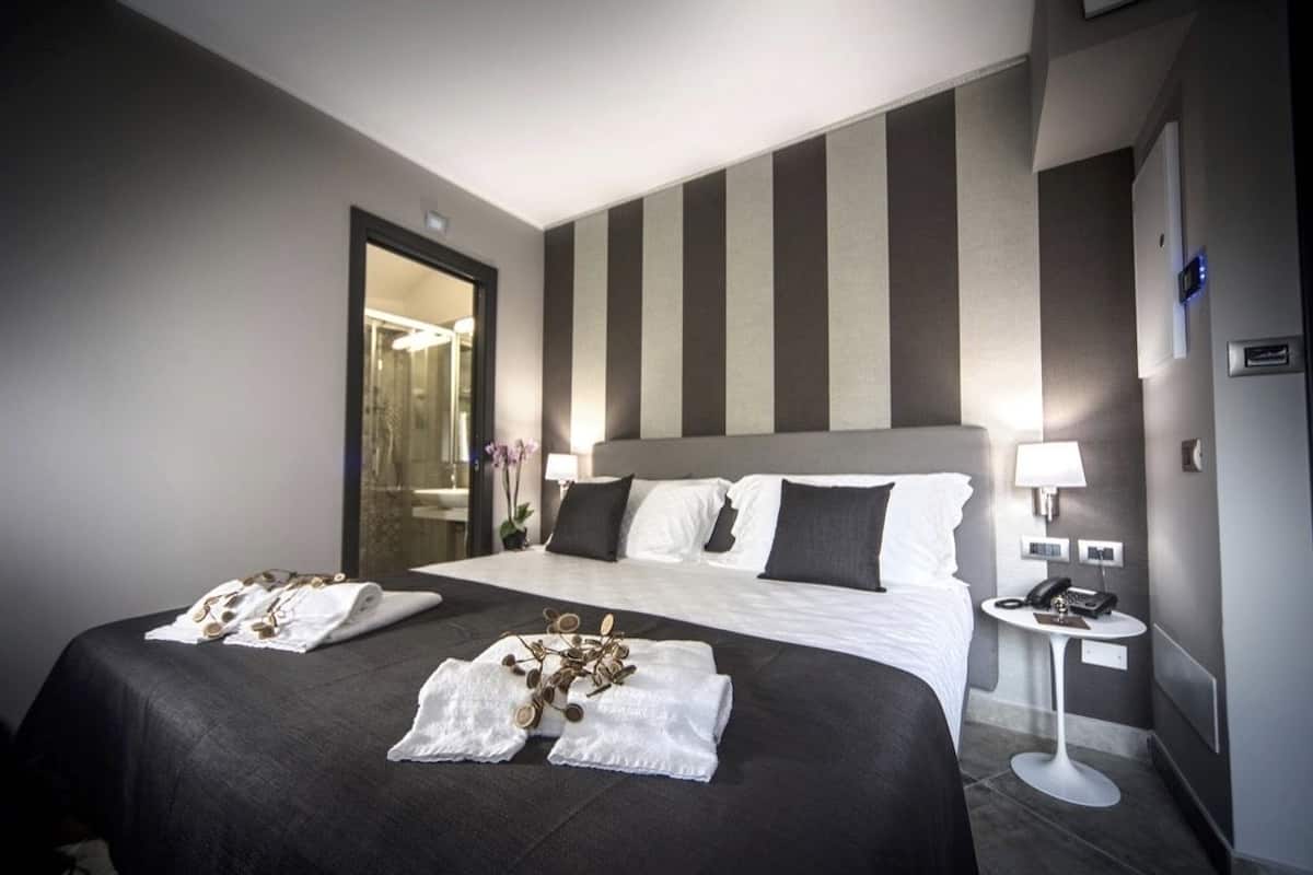 A hotel room with two beds, a bedside table with a lamp, and a mirror.