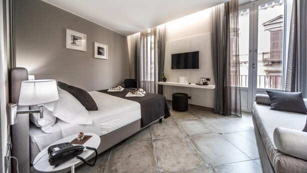 A modern hotel room with a bed, bedside table, lamp, phone, and a sofa. - Etnea 454   Catania Luxury Rooms (Catania)