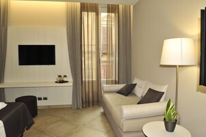 A modern hotel room with a sofa, a flat-screen TV, a lamp, and a potted plant.