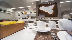 A modern dining area with a table set for breakfast, including plates, cups, and a teapot. - Etnea 454   Catania Luxury Rooms (Catania)
