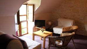 Una habitación acogedora con pared de piedra, cama, televisor, mesa con un florero y sillas de mimbre.