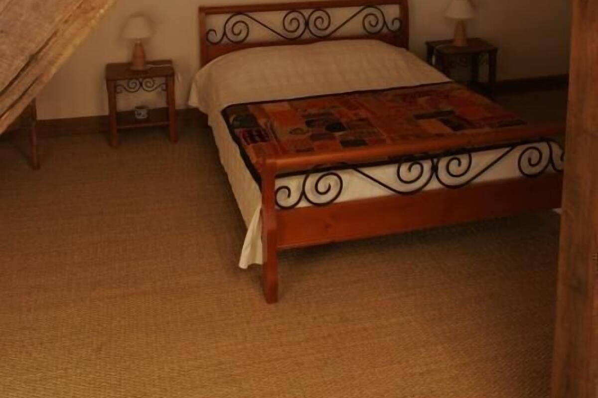 Un dormitorio con techo de madera, una cama con edredón estampado, una araña y una pequeña mesa con lámpara.
