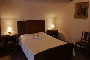 Ein ordentlich bezogenes Bett mit Holz-Kopfteil, zwei Nachttische mit Lampen, ein Sessel und ein Gemälde an der Wand.