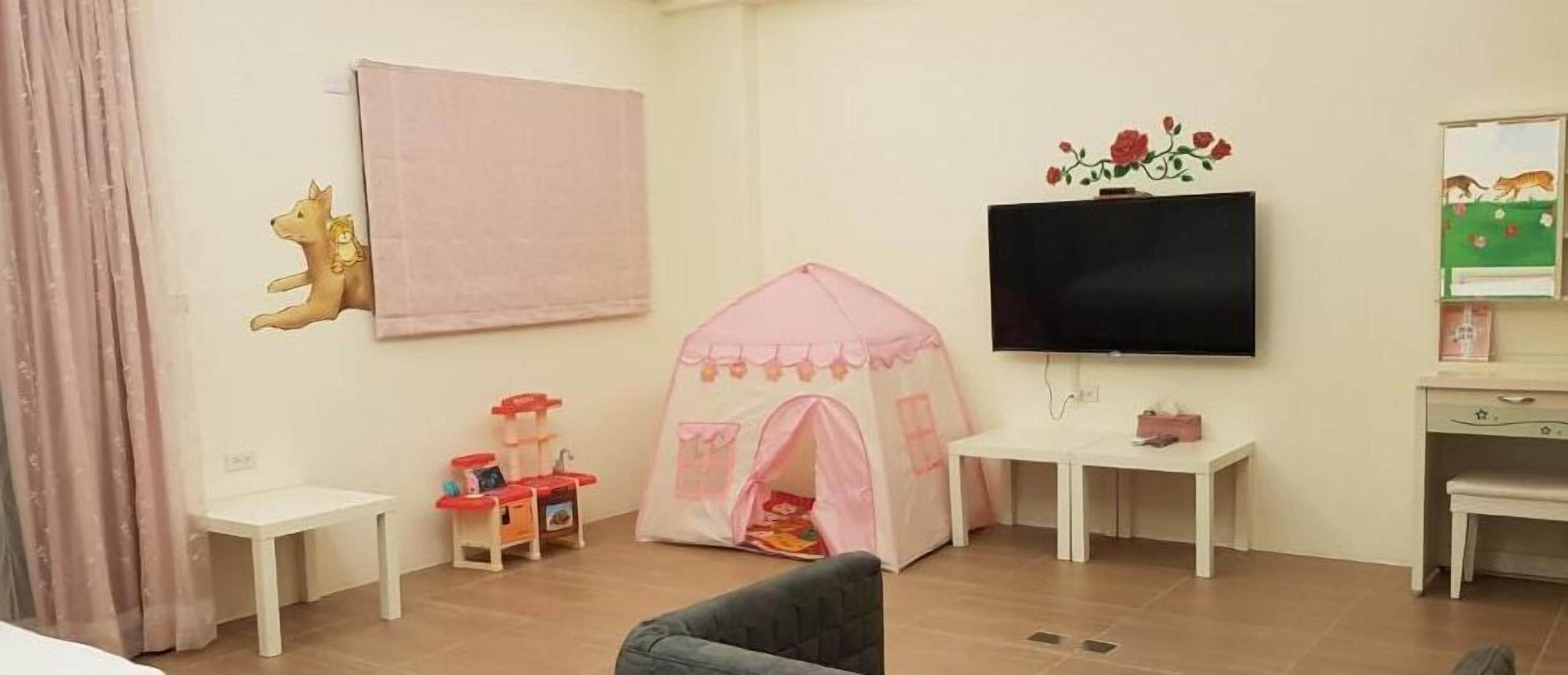 A child-friendly living room with a play tent, a flat-screen TV, and a small table.