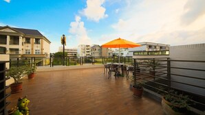 A rooftop terrace with a wooden floor, outdoor seating, and potted plants. - Rose Cottage B&B (Taitung)