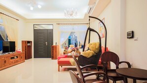 A living room with a sofa, a hanging chair, a TV, and a dining table. - Rose Cottage B&B (Taitung)