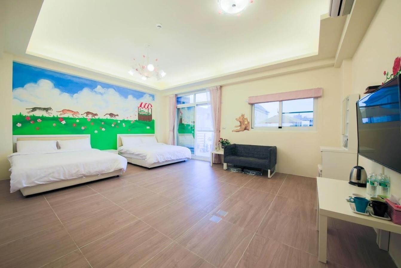 A hotel room with two beds, a sofa, a TV, and a mural on the wall.