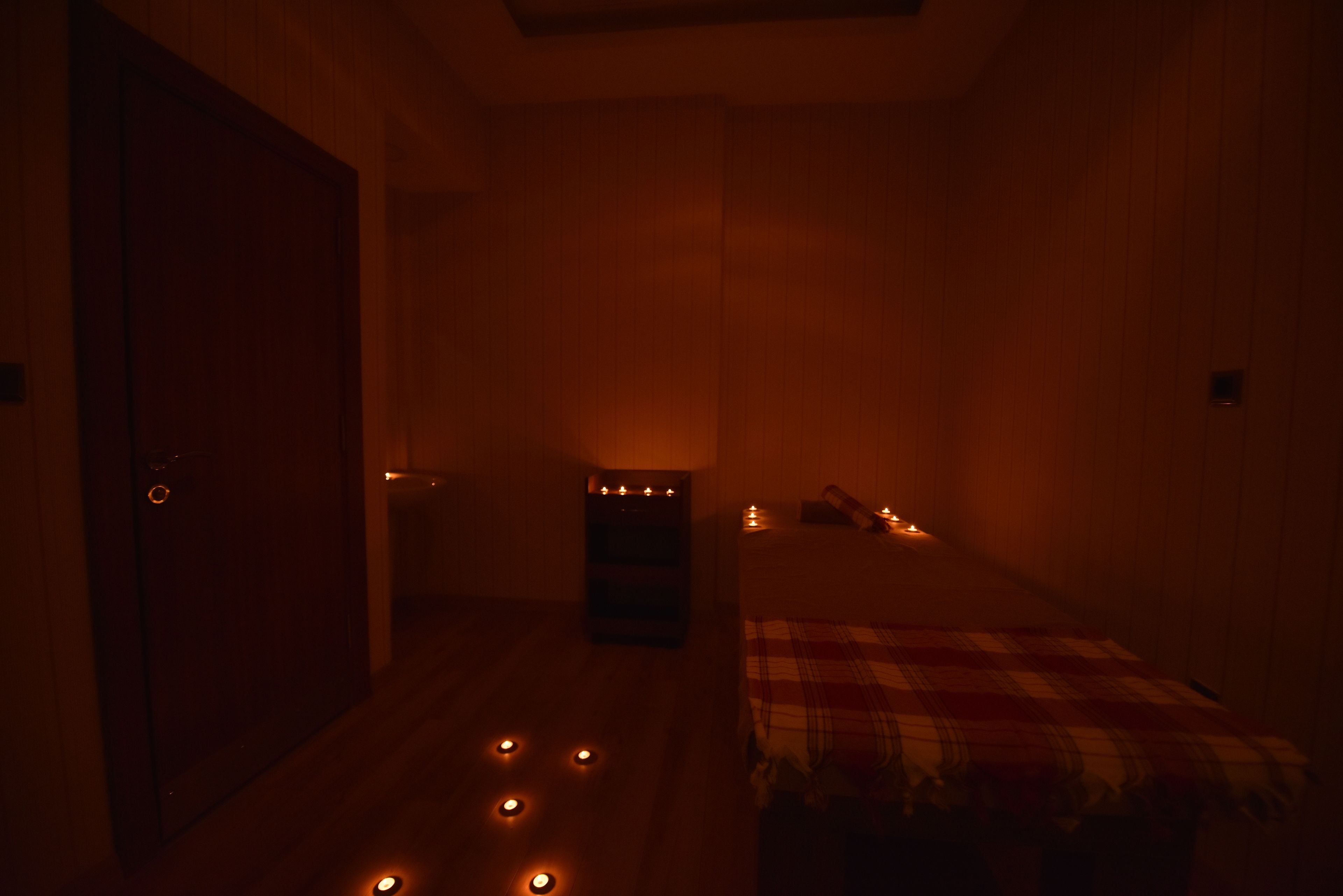 A dimly lit room with a bed, a wooden wardrobe, and several lit candles on the floor.