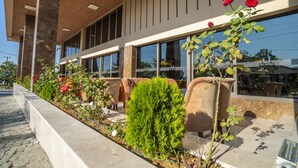 Een modern gebouw met grote ramen, terras en een tuin vol planten en bloemen.