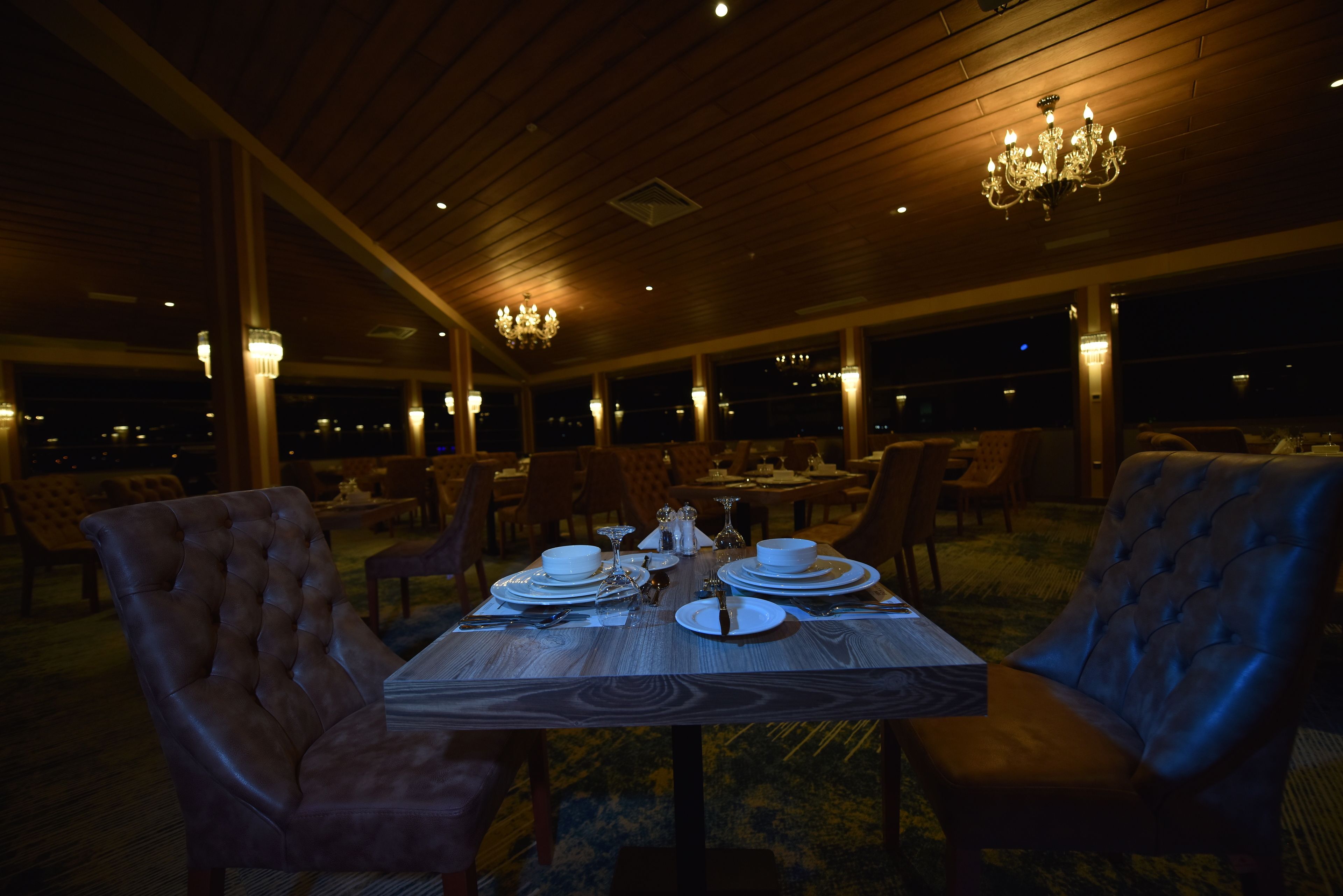 Comedor con una mesa de madera dispuesta para cuatro personas, rodeada de sillas tapizadas, bajo un techo de madera con candelabros.