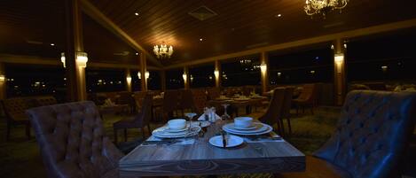 Comedor con una mesa de madera dispuesta para cuatro personas, rodeada de sillas tapizadas, bajo un techo de madera con candelabros.