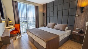 Een moderne hotelkamer met een groot bed, een bureau met stoel, een bureaulamp en uitzicht op de stad.