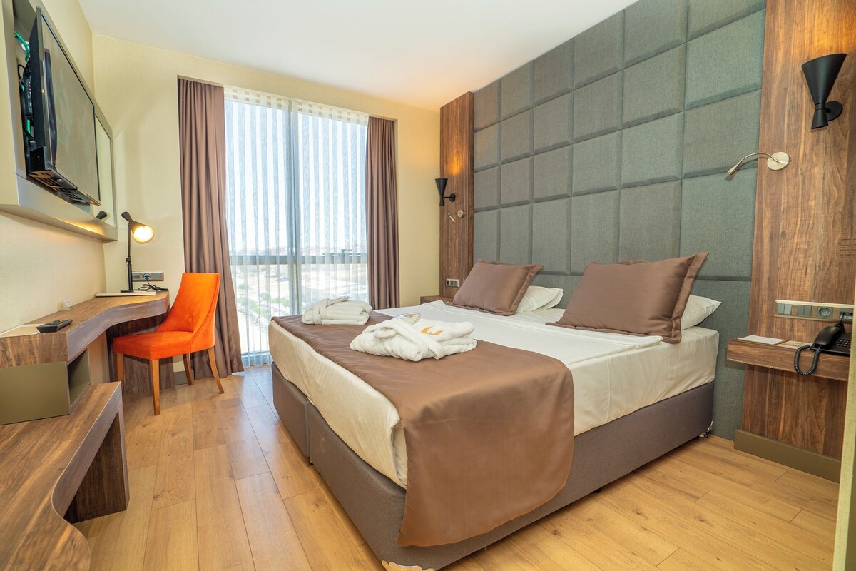 A hotel room with a bed, a desk, a chair, a TV, and a window with curtains.