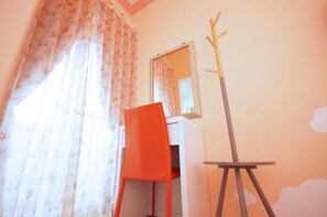 A room with a desk, a chair, a mirror, and a coat rack.