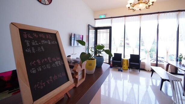 A modern hotel lobby with a wooden reception desk, a chalkboard menu, a large clock, and a chandelier. - Man Lu B&B (Hualien City)