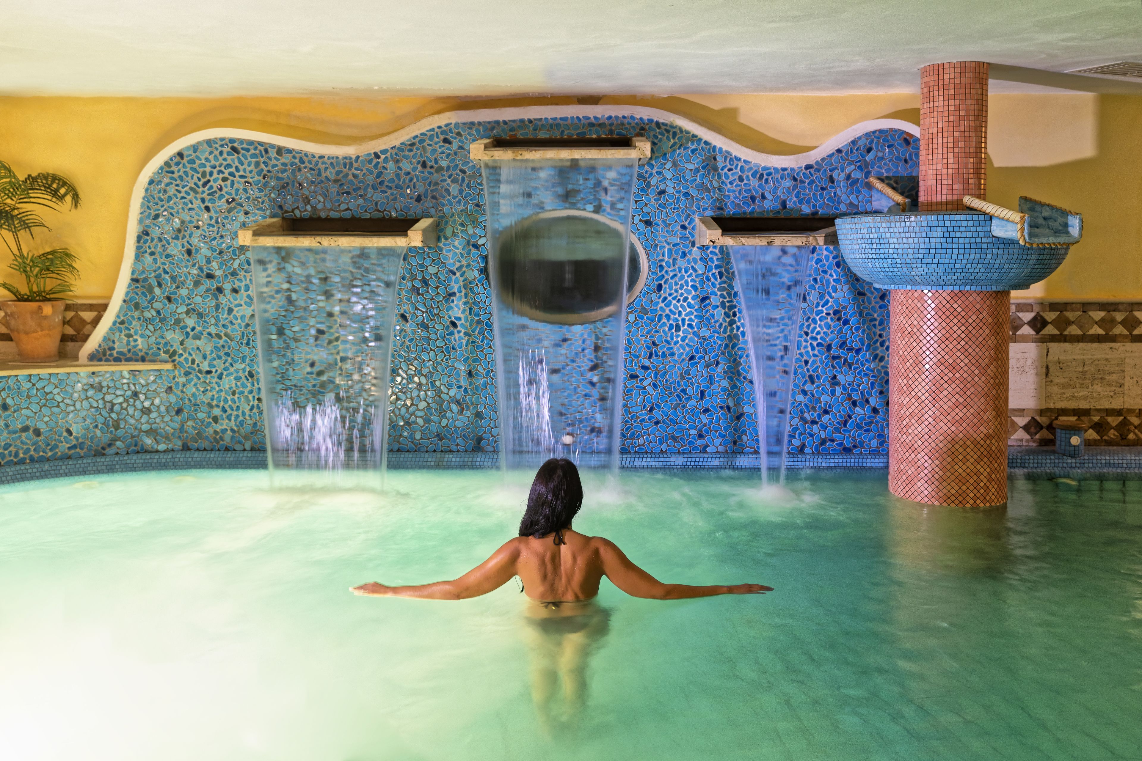 Una persona en una piscina con una fuente decorativa y paredes con mosaicos.