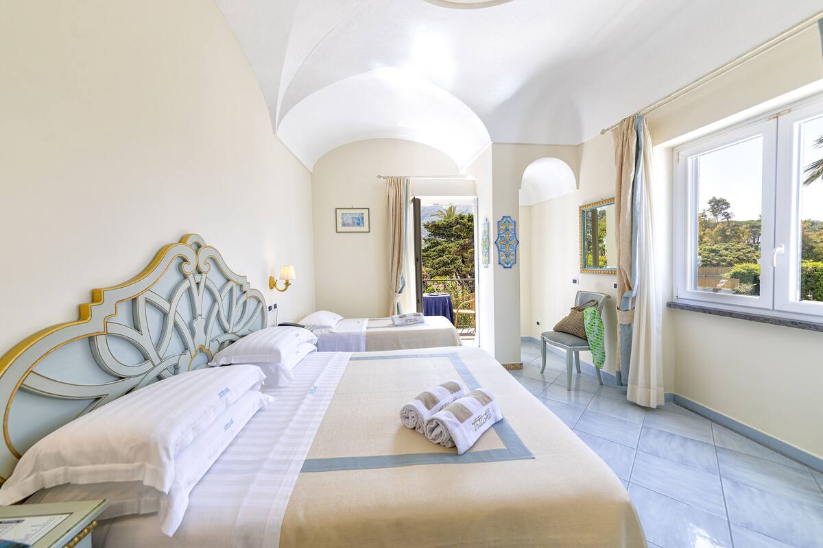 A hotel room with two beds, a balcony, and a view of the outdoors.