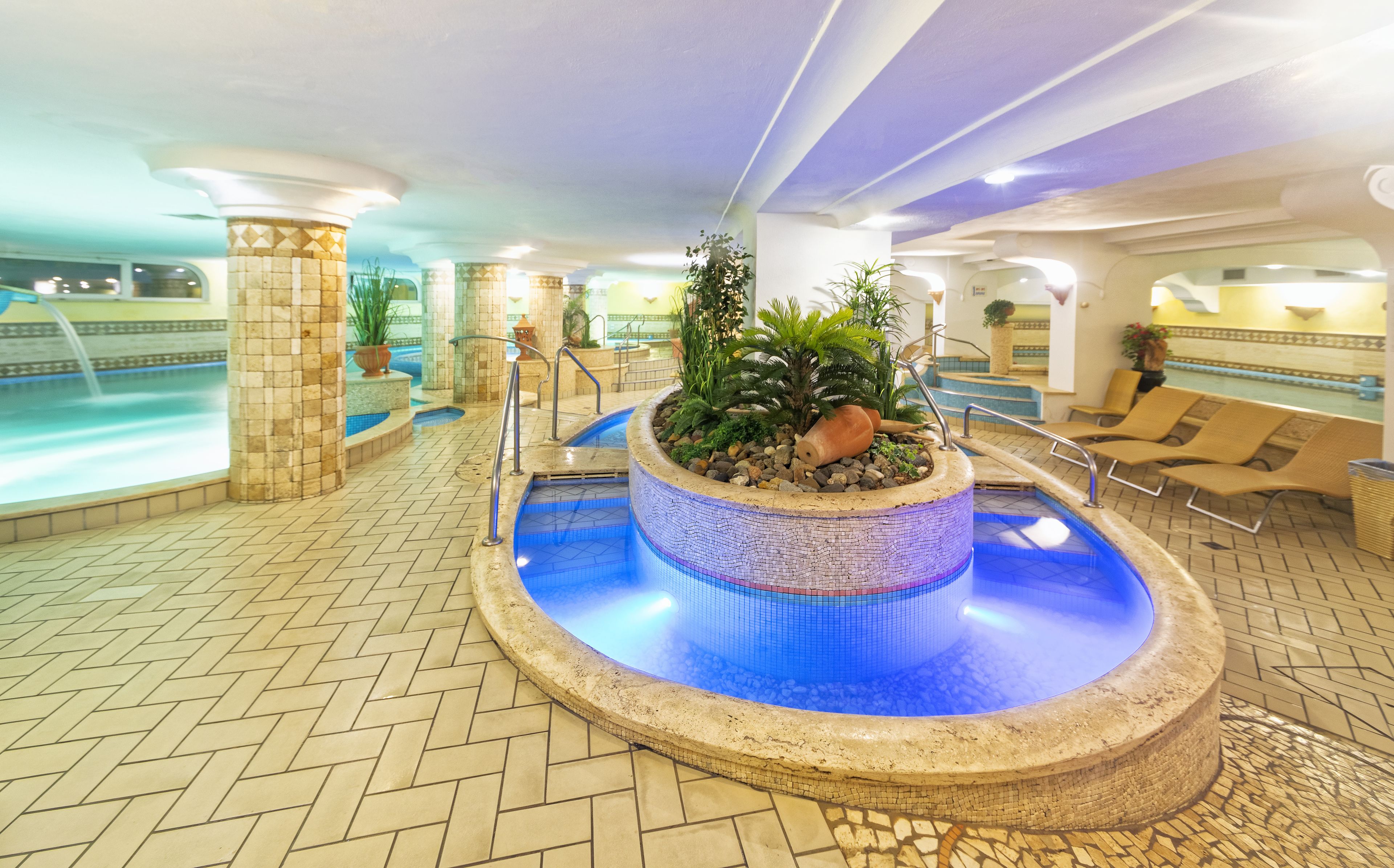 A pool area with a mosaic-tiled hot tub surrounded by lounge chairs and potted plants.