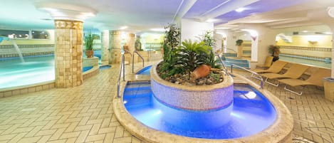 A pool area with a mosaic-tiled hot tub surrounded by lounge chairs and potted plants.