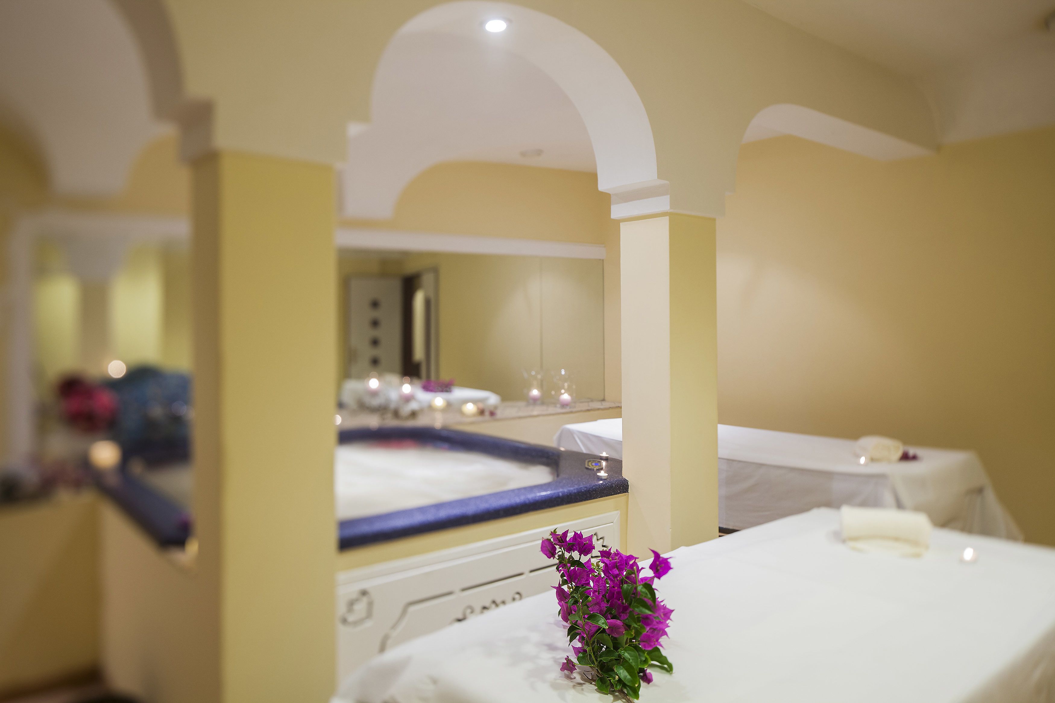 Ein Spa-Raum mit einer Badewanne, einem Spiegel und einem kleinen Tisch mit einer Blume.