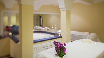 Ein Spa-Raum mit einer Badewanne, einem Spiegel und einem kleinen Tisch mit einer Blume.