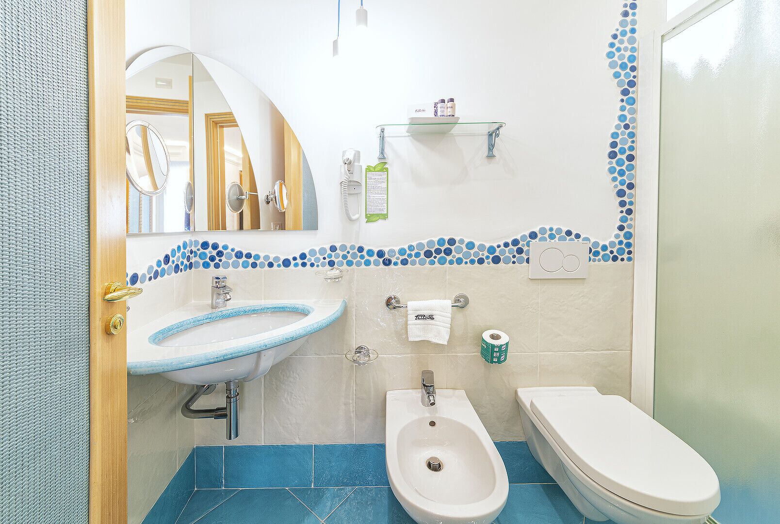 A bathroom with a sink, bidet, and toilet, a mirror, and a shelf with toiletries.