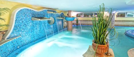 Un área de piscina con una pared de mosaicos azules, una fuente de agua y una planta en maceta.