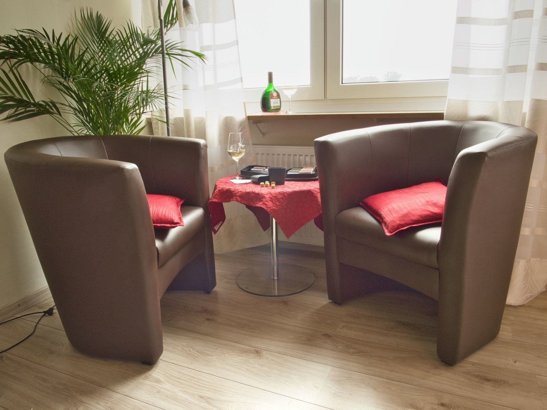 A room with two leather armchairs, a small table with a red tablecloth, a bottle, and a glass of wine.