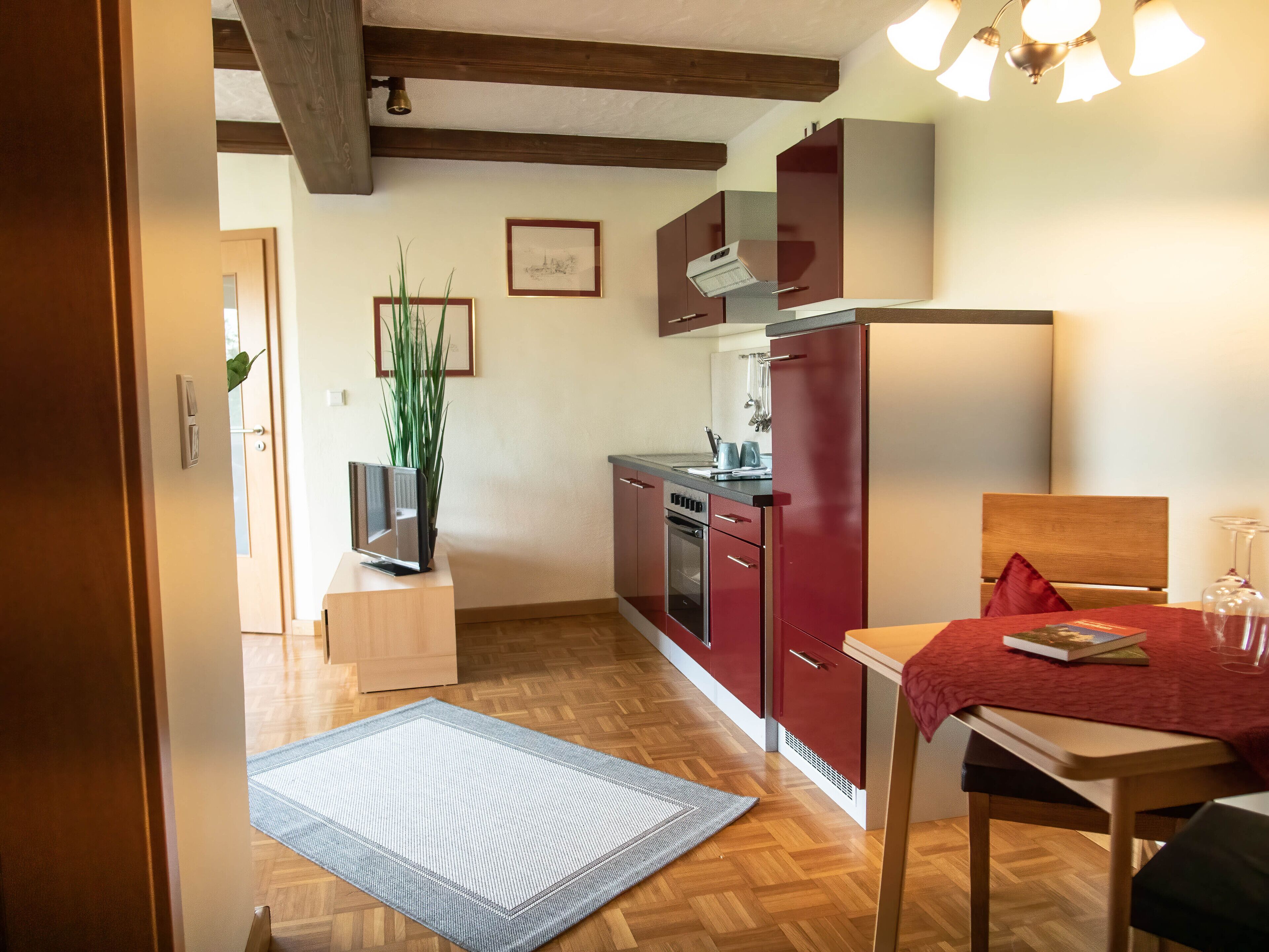 A compact kitchen with wooden flooring, a dining area with a table and chairs, and a small rug.