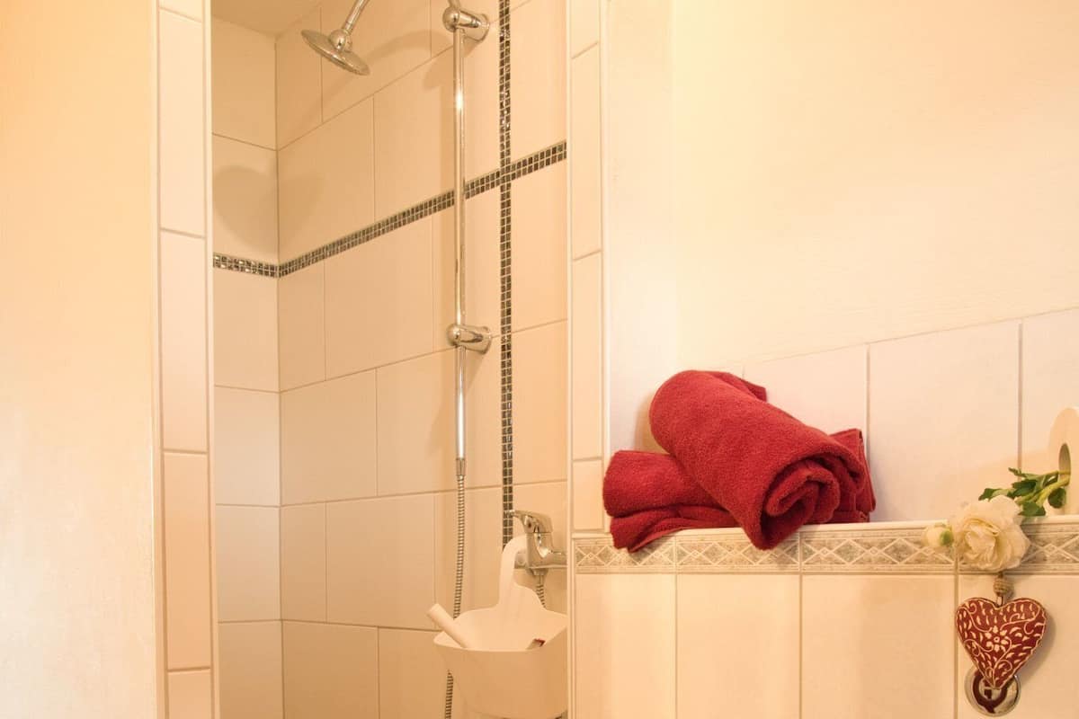 A shower with a handheld showerhead, a towel rack with a red towel, and a heart-shaped decoration on the wall.