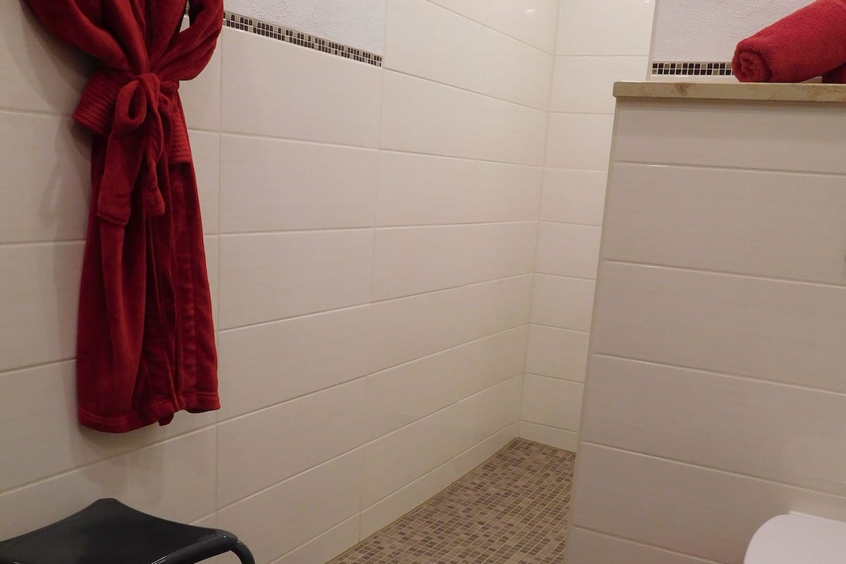 A bathroom with white tiled walls, a black metal chair, a red bath mat, and a red towel on the floor.