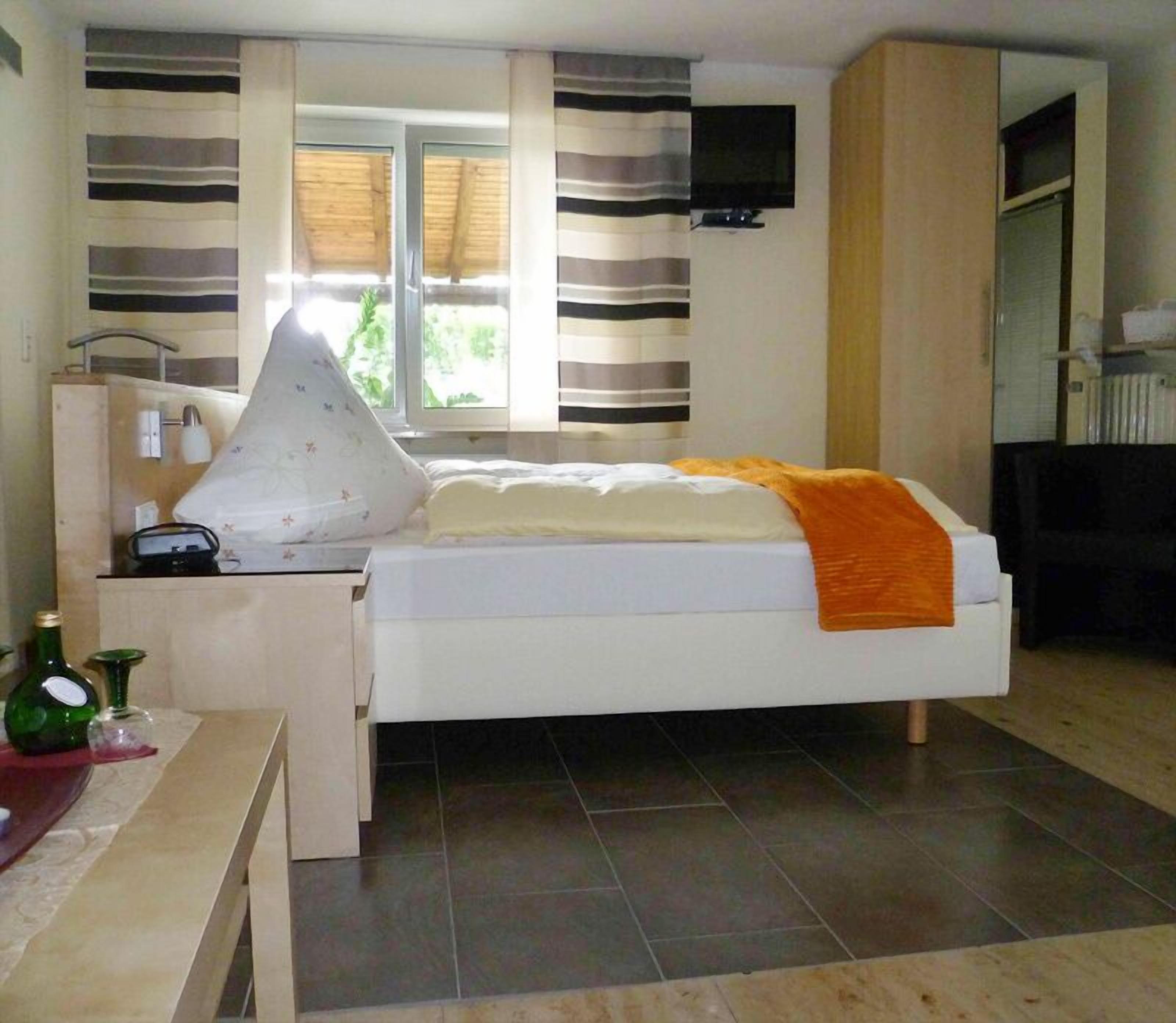 Ein Schlafzimmer mit Bett, Nachttisch mit Lampe, Wand-TV und einem Vorhangfenster.