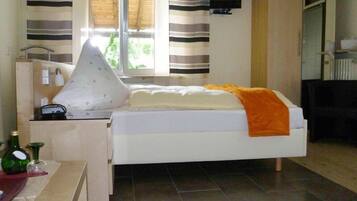 Ein Schlafzimmer mit Bett, Nachttisch mit Lampe, Wand-TV und einem Vorhangfenster.