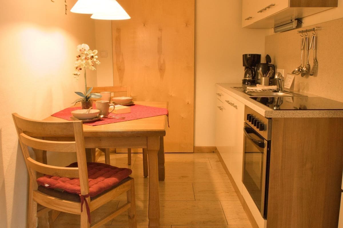 A compact kitchen with a dining table, chairs, a hanging light, and basic appliances.