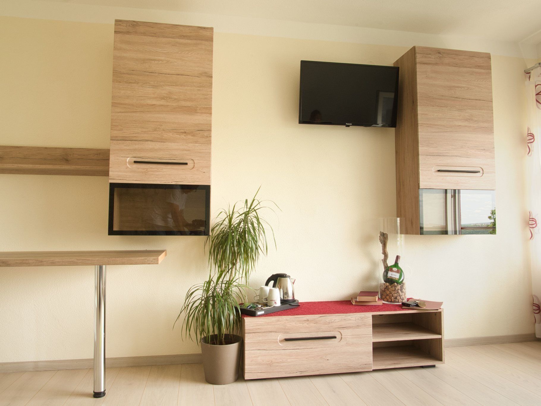 A modern kitchen with wooden cabinets, a built-in TV, a potted plant, and a red countertop.