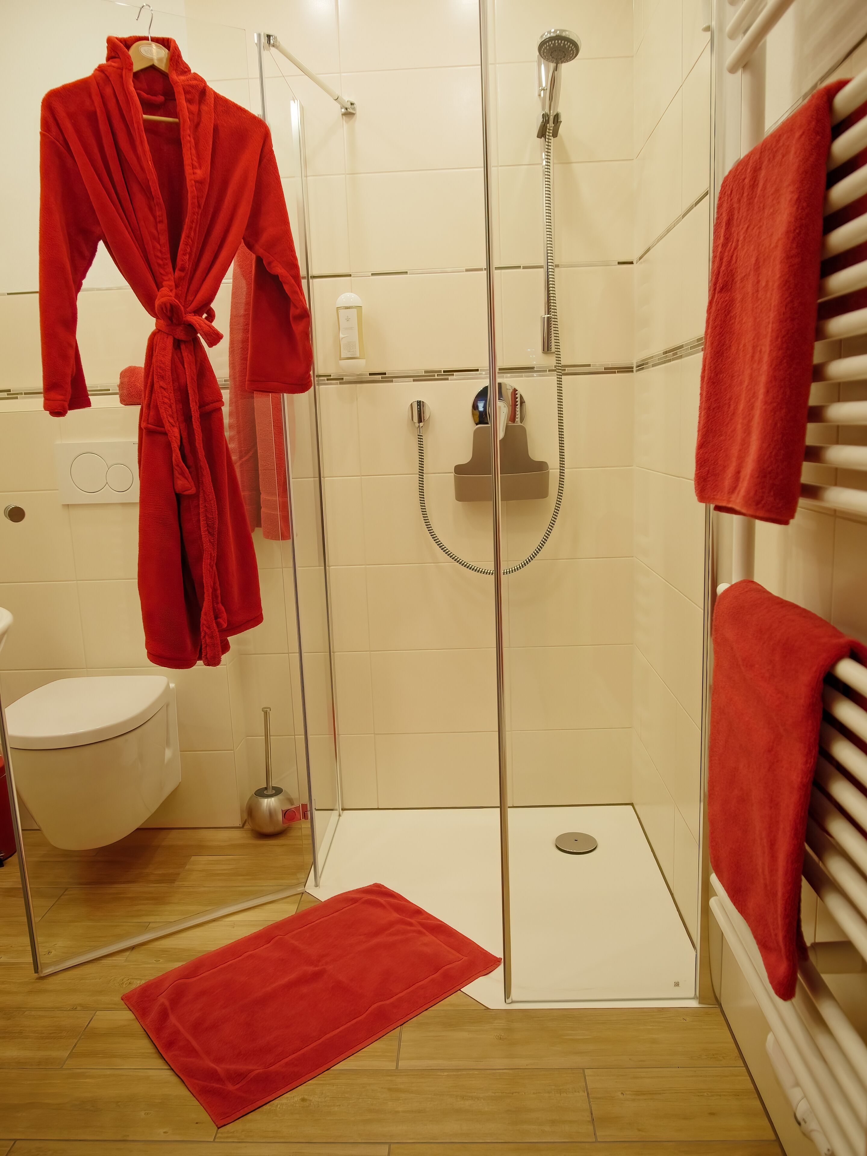 A bathroom with a glass-enclosed shower, a white toilet, and a red bathrobe hanging on a rack.