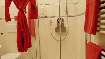 A bathroom with a glass-enclosed shower, a white toilet, and a red bathrobe hanging on a rack.