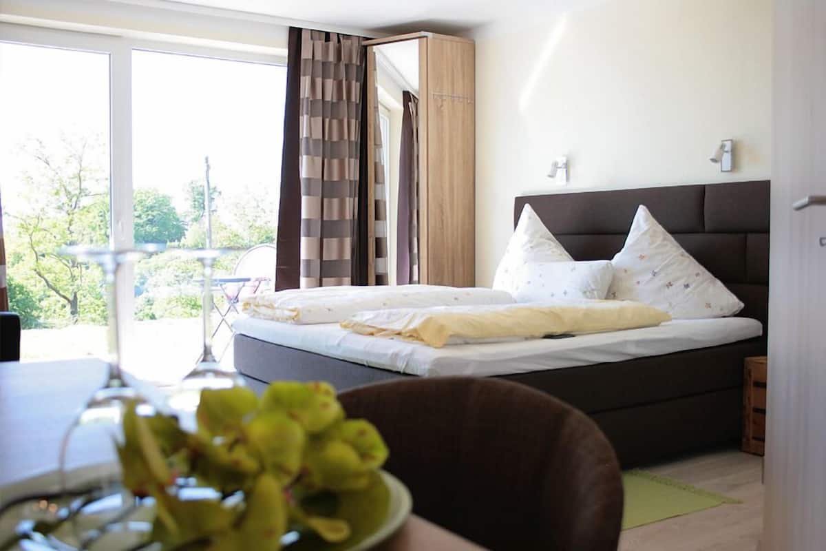 A bedroom with a large bed, a window with curtains, and a view of trees outside.