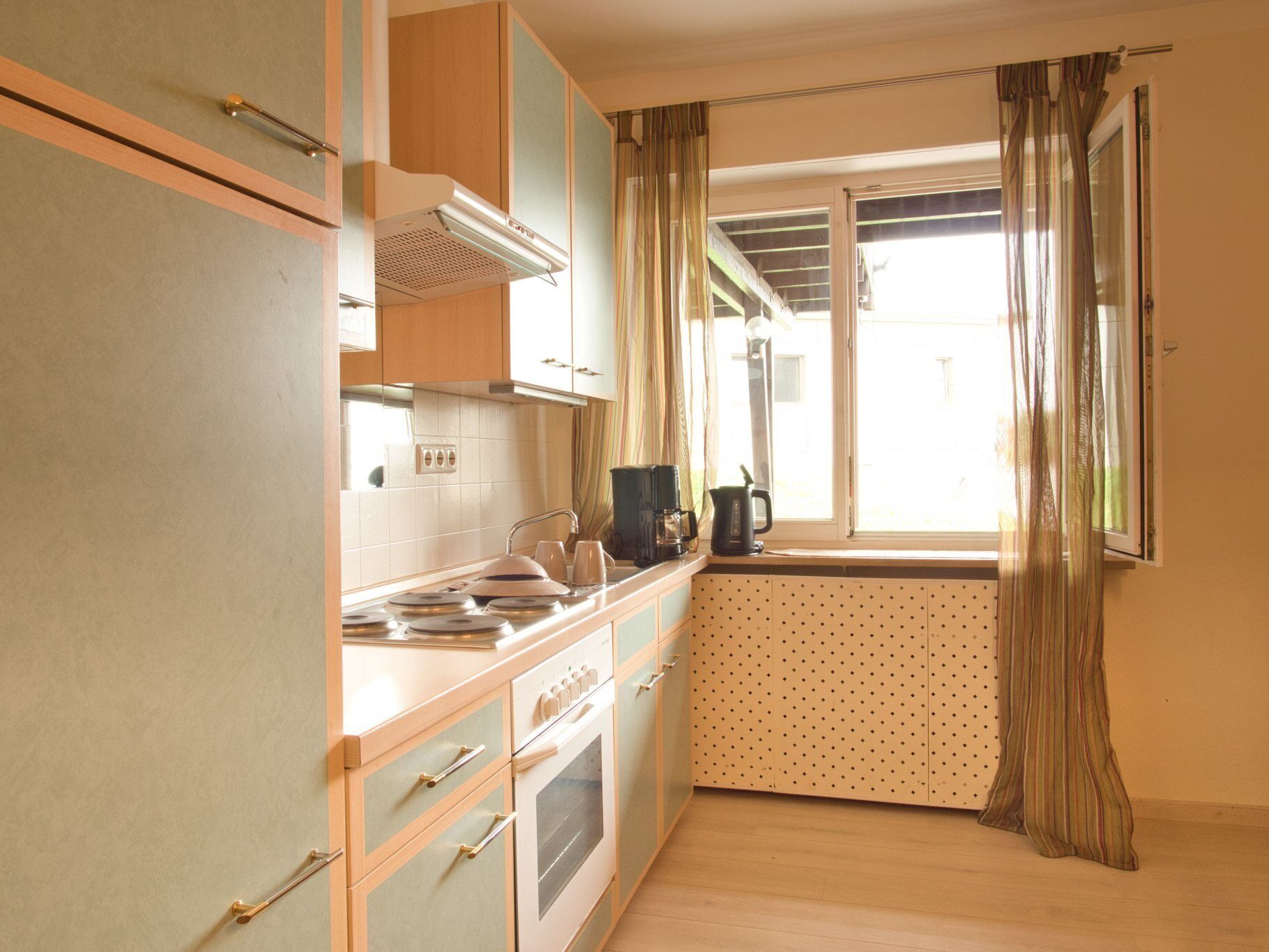 A compact kitchen with a stove, sink, and a window with curtains.