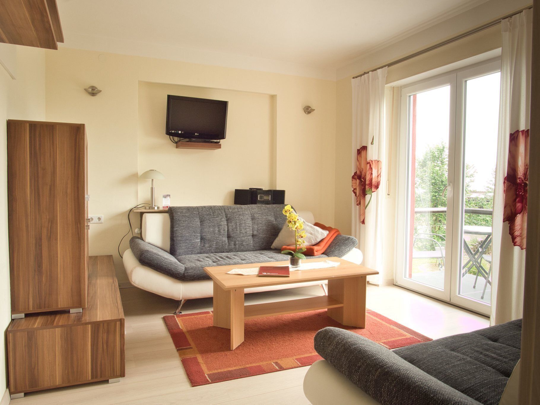 Ein modernes Wohnzimmer mit Sofa, Couchtisch, Fernseher und einer Schiebetür zum Außenbereich.