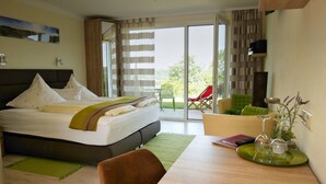 A hotel room with a bed, a dining table, a chair, a plant, and a view of the outdoors. - Kirschberghof - Adults Only (Sommerhausen)