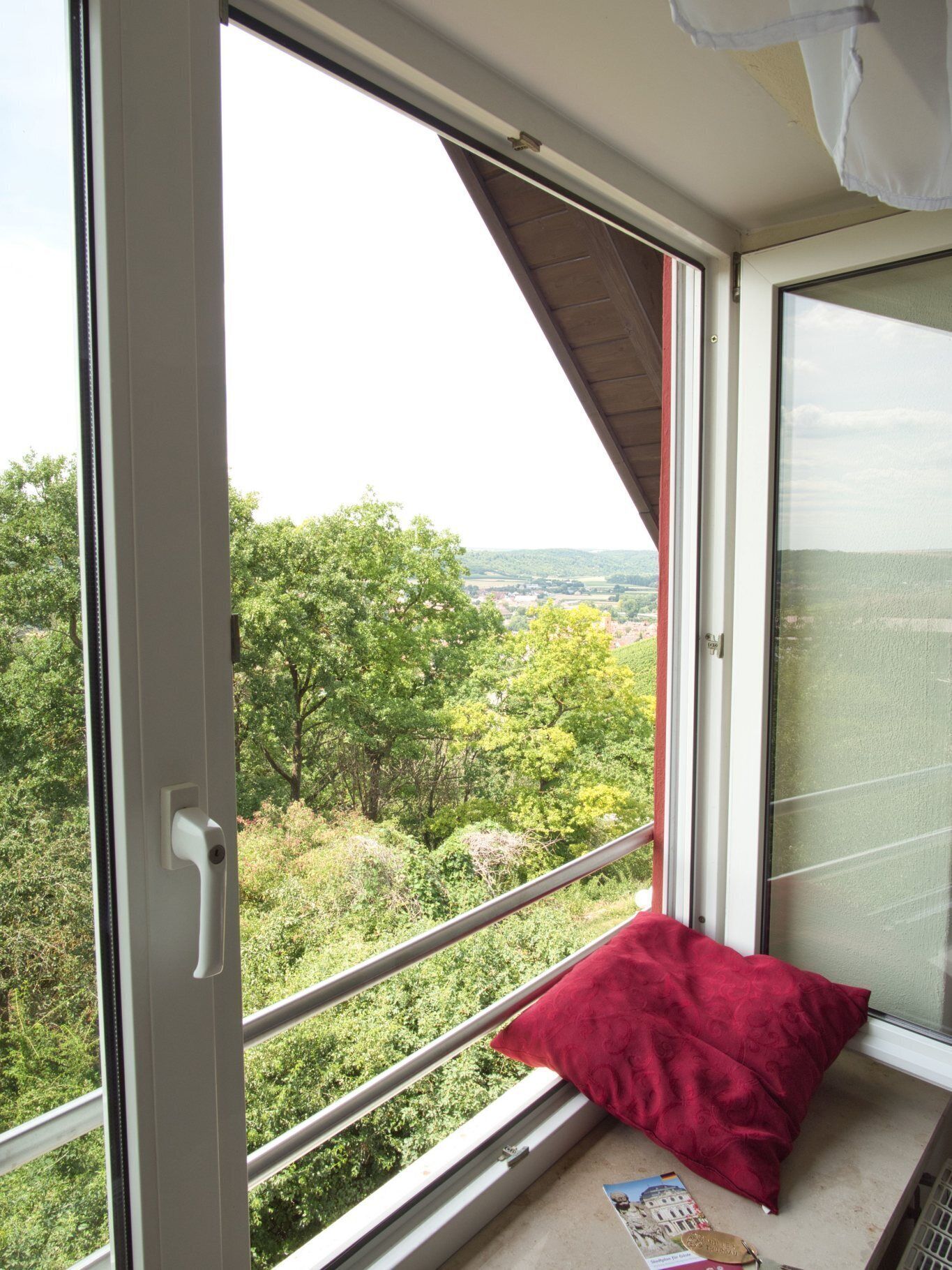 Une pièce avec une grande fenêtre, un coussin rouge et un magazine posé sur le rebord de la fenêtre.